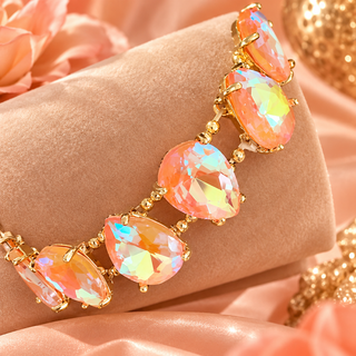 Peach iridescent crystal tennis bracelet with gold-tone prong settings on velvet display