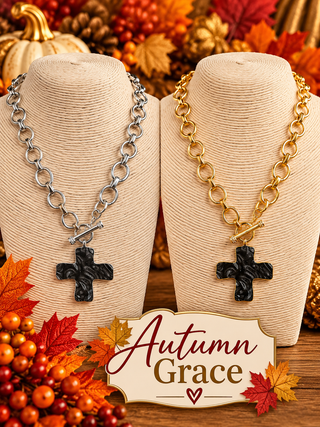 Silver and gold chain-link necklaces with black textured cross pendants on display busts