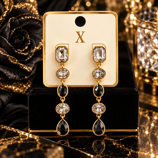 Long gold-tone drop earrings with clear and black bezel-set crystal stones on display card