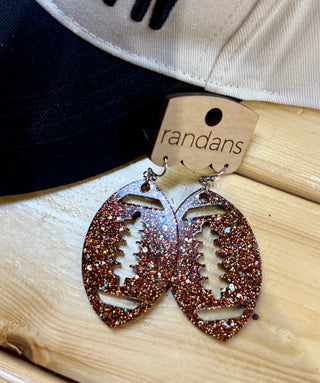 Glitter copper football-shaped dangle earrings with cut-out lace detail on wooden display