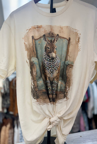 Cream graphic tee featuring a bejeweled donkey seated in a teal wingback chair