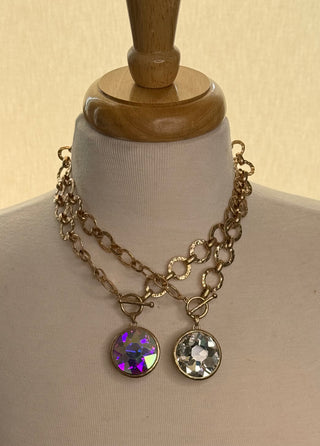 Two gold-tone chain necklaces with large faceted crystal pendants, one iridescent purple, one clear