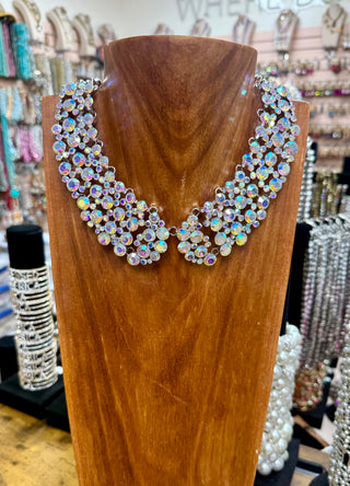 Wide iridescent rhinestone bib collar necklace with silver-tone framework on wooden display