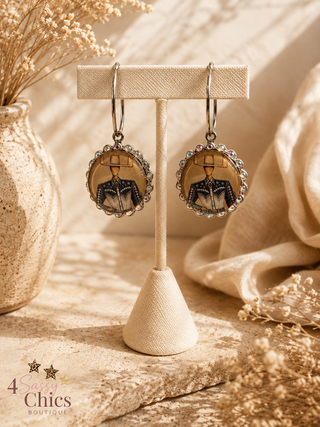 Western cowboy illustrated dangle hoop earrings with rhinestone scalloped bezel on display stand