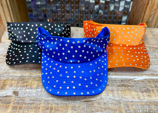 Rhinestone-studded sun visors in royal blue, black, and orange on a wood surface