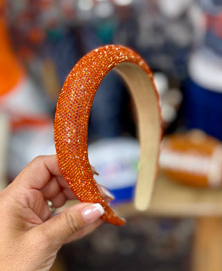 Orange rhinestone-covered wide padded headband held up against blurred background
