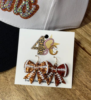 Glitter sequin football bow dangle earrings with white stitch details on card