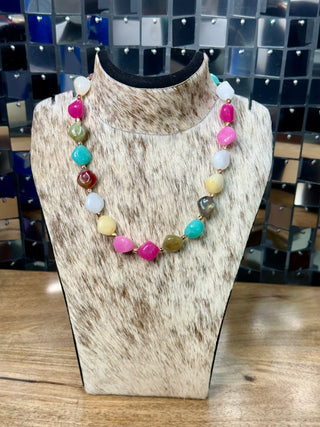 Multicolor polished stone beaded necklace with gold-tone spacers on cowhide display bust