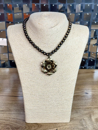 Dark brown beaded necklace with large bronze floral rosette pendant on display bust