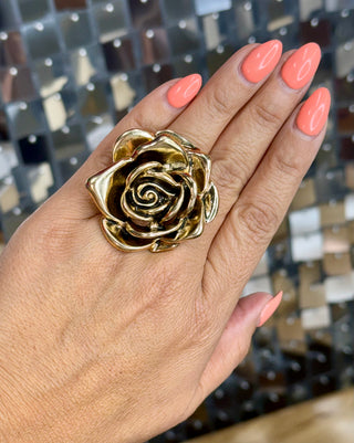 Oversized gold rose cocktail ring worn on palm of hand with coral nails