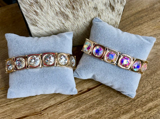 Two gold-tone stretch bracelets with large round crystal and iridescent AB stones on display pillows