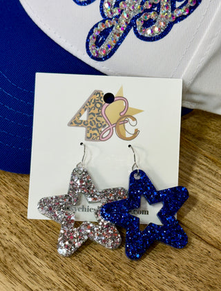 Mismatched glitter star dangle earrings, one silver and one royal blue, on display card