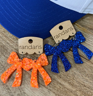 Glitter bow dangle earrings in orange and royal blue on wooden display cards