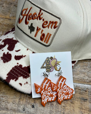 Burnt orange Texas-shaped Hook Em Horns earrings with silver bow charms on display card