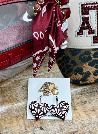 Burgundy heart-shaped dangle earrings with white Talavera floral pattern on display card