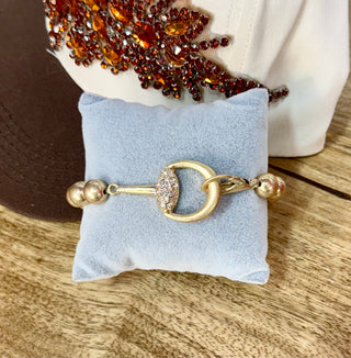 Gold-tone bangle bracelet with pavé rhinestone equestrian snaffle-bit centerpiece on velvet pillow