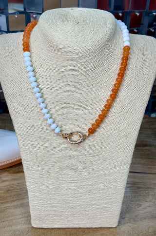 Two-tone orange and white beaded necklace with gold carabiner clasp on display bust