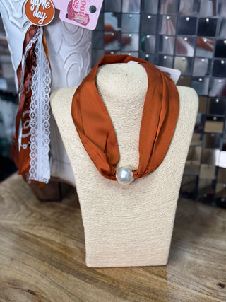 Burnt orange satin infinity scarf with large pearl accent on jewelry display bust