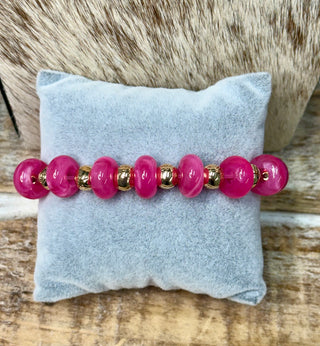 Fuchsia pink beaded stretch bracelet with gold metallic spacers on gray velvet pillow
