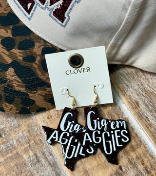Maroon glitter Texas-shaped dangle earrings reading Gig em Aggies on jewelry card
