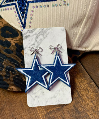 Blue glitter star dangle earrings with silver bow studs on marble display card
