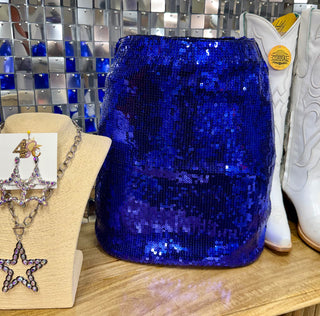 Royal blue sequin mini skirt displayed on wooden shelf with white cowboy boots