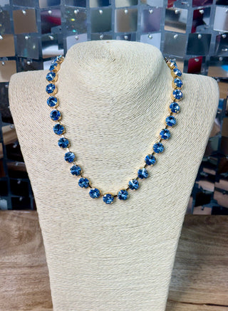 Blue crystal rhinestone tennis necklace with gold-toned pronged settings on display bust