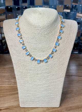Gold-tone collar necklace with light blue rectangular stones and clear rhinestones on display bust