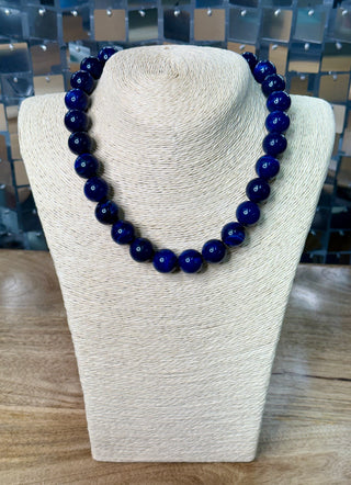 Glossy navy blue round bead single-strand necklace displayed on cream jewelry bust