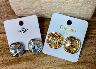 Two pairs of cushion-cut crystal stud earrings in silver and gold tones on display cards