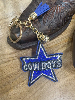 Blue rhinestone Cowboys star keychain with gold chain, tassel, and cowboy boot backdrop