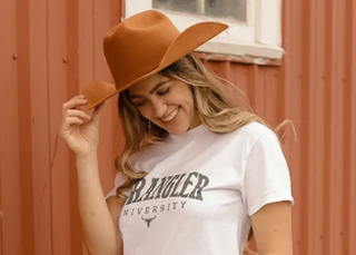 Tan wide-brim cattleman cowboy hat worn by smiling blonde woman in white tee